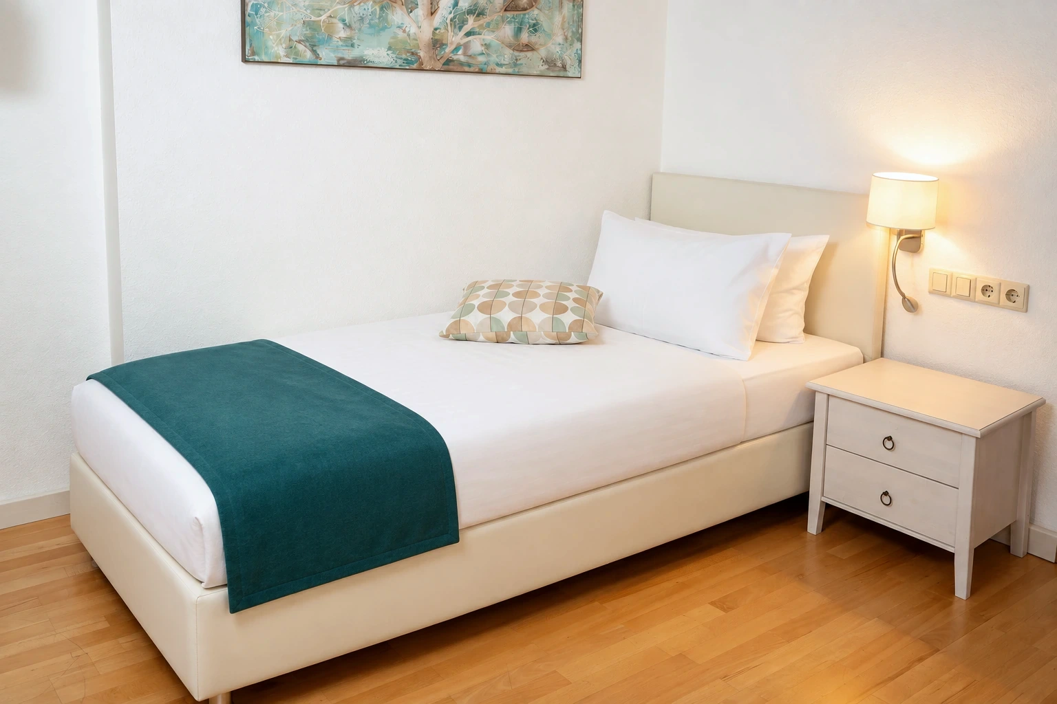 Einzelzimmer mit hellem Bett und türkisfarbenem Überwurf