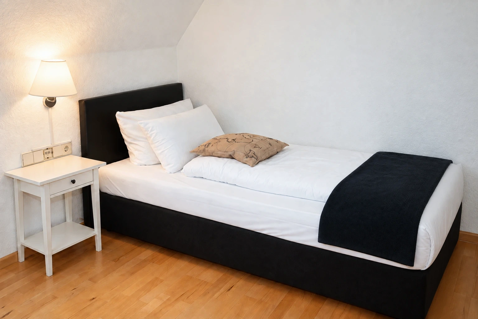 Einzelzimmer mit schwarzem Bett und hellem Holzfußboden