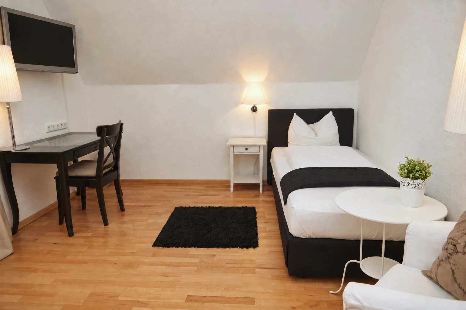 Einzelzimmer mit schwarzem Bett und Schreibtisch